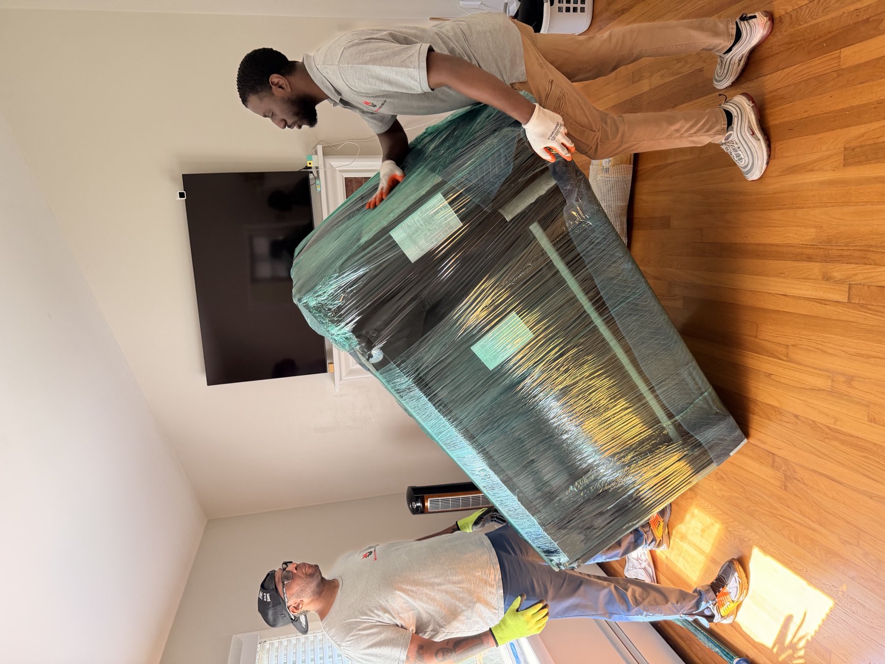 Two Major Movers crew members carrying a shrink-wrapped sofa through a living room