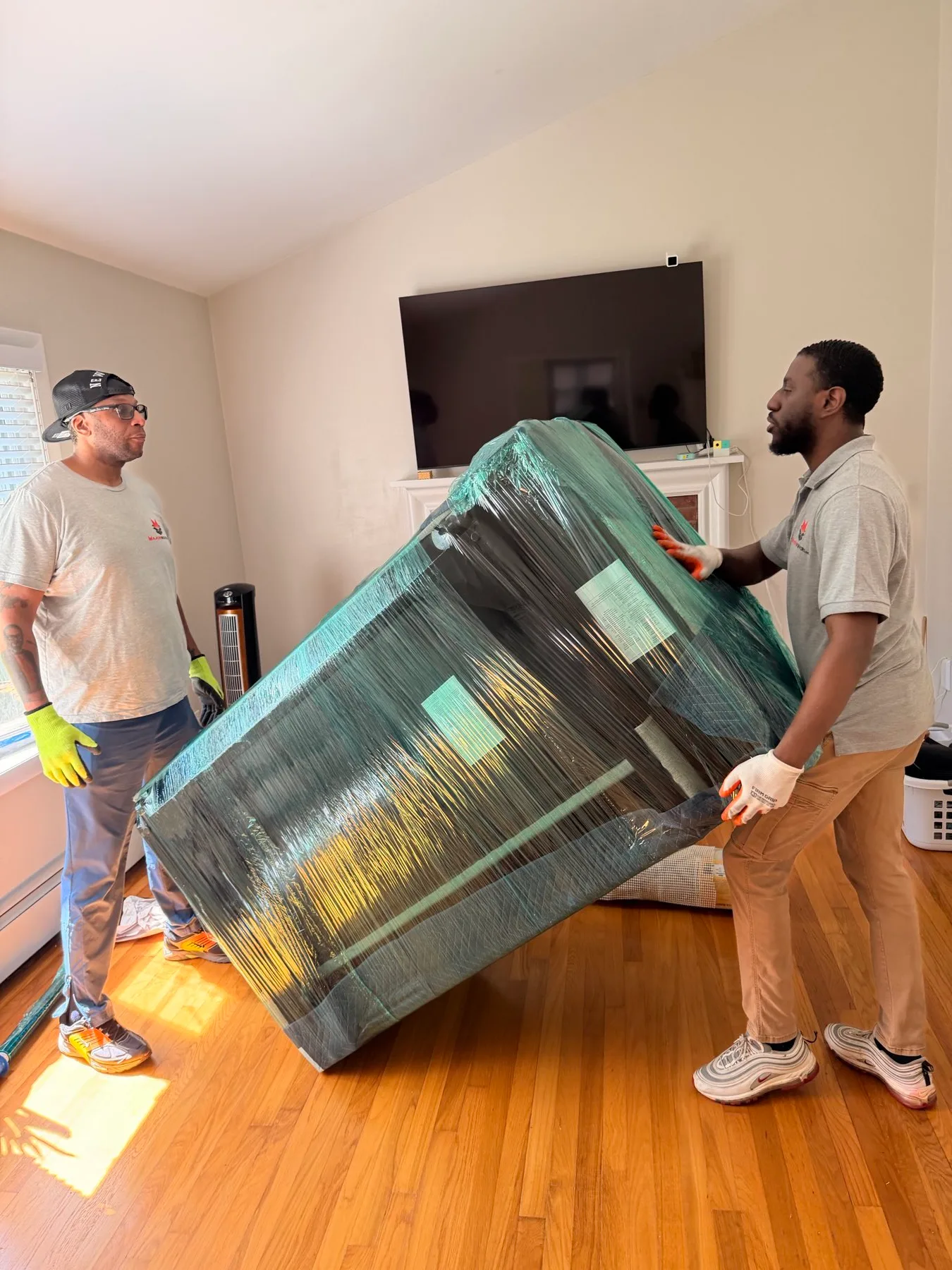 Two Major Movers crew members carrying a wrapped sofa through a living room